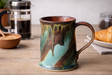 Handmade pottery mug with turquoise and copper glaze on kitchen table, French press coffee