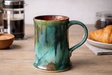  Handmade ceramic mug in teal green and rust glaze on wooden surface, Buxton Pottery Australia