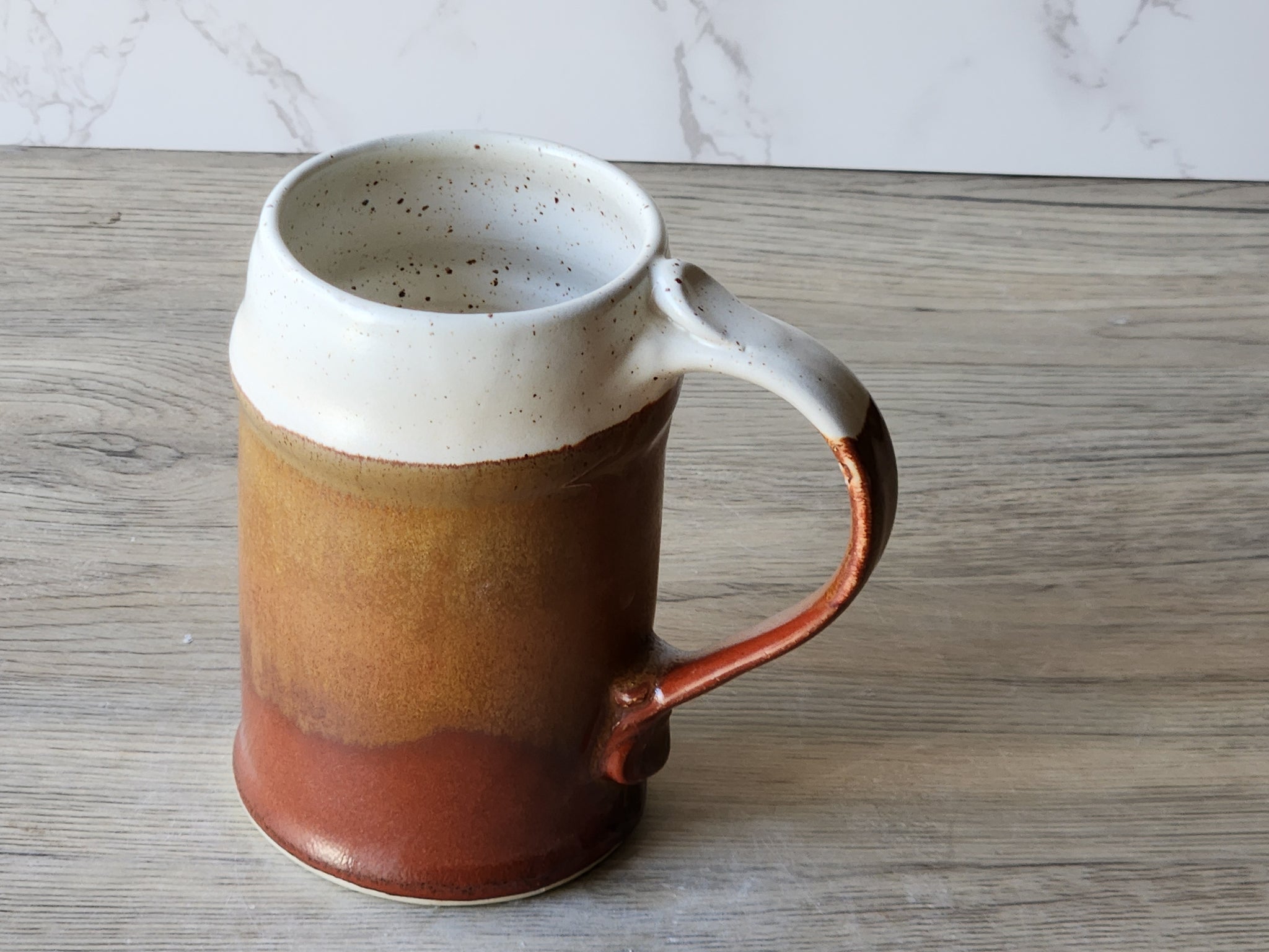 Wheel-thrown stoneware beer mug in cream with rich brown glaze pour