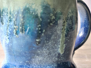 Close up of Handmade blue and green ceramic mug with ash glaze drips