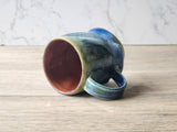 Handmade blue and green ceramic mug with ash glaze drips  on its side, interior shown