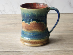 Handmade ceramic mug with multicolored glaze on a wooden surface.