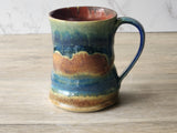 Handmade ceramic mug with multicolored glaze on a wooden surface.