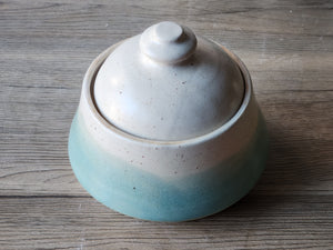 Ceramic lidded jar with a cream and green glaze on a wooden surface