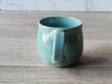 handle view of Glazed handmade stoneware coffee cup with subtle colour variation in blue-green