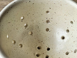 Close up of glaze on a Unique ceramic colander bowl in speckled cream glaze
