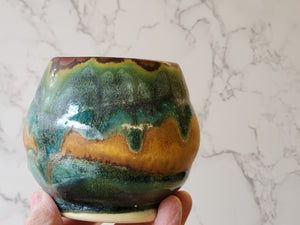Hand holding a Handmade ceramic yunomi cup with earthy brown and green Glazes.
