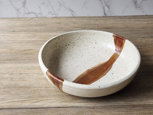 Rustic ceramic bowl with speckled cream glaze and brown accent