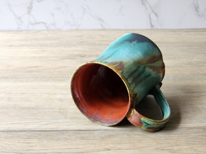 Internal view of a 400 ml handmade ceramic mug with a ed brown glossy internal glaze and a multi coloured external glaze in light and deep turquoise and tan and brown. 