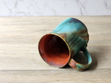 Internal view of a 400 ml handmade ceramic mug with a ed brown glossy internal glaze and a multi coloured external glaze in light and deep turquoise and tan and brown. 