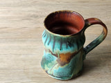Handmade Artisan ceramic cup showing earthy glaze detail, in turquoise and brown.