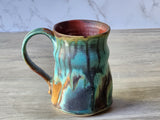 Side view of wheel-thrown mug with variegated drippy glaze