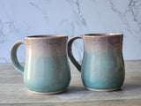 Two handmade pottery mugs with soft green and neutral glaze, wheel-thrown stoneware mugs