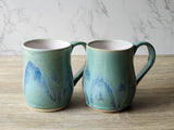 Pair of handmade ceramic mugs with blue and green glaze on wooden surface”