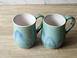 Handcrafted stoneware mugs with ocean-inspired blue green glaze, side view.