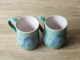 “Top view of handmade pottery mugs with glossy blue green glaze”