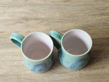 Handmade stoneware mug with soft green and blue glaze and glossy white interior