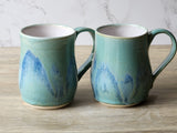 “Matching handmade coffee mugs with soft blue green glaze on kitchen bench”