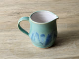 Small handmade stoneware jug for milk or cream on wooden surface
