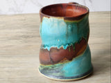 Handmade pottery mug showing organic glaze movement in turquoise and rust tones”