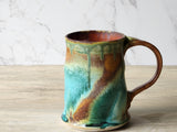 Handmade ceramic mug with turquoise and rust glaze on wooden surface