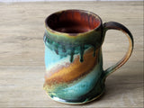 Handmade ceramic coffee mug showing iron red interior glaze and teal ochre landscape band, Buxton Pottery