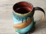 One of a kind handmade ceramic mug with sculpted ripples and dark green drip glaze over teal and ochre