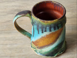 Handmade pottery mug showing iron-red interior glaze and dark drip detail on rim