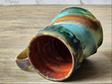 Handmade ceramic mug angled view showing iron red interior, glossy drip rim and teal ochre glaze, Australia