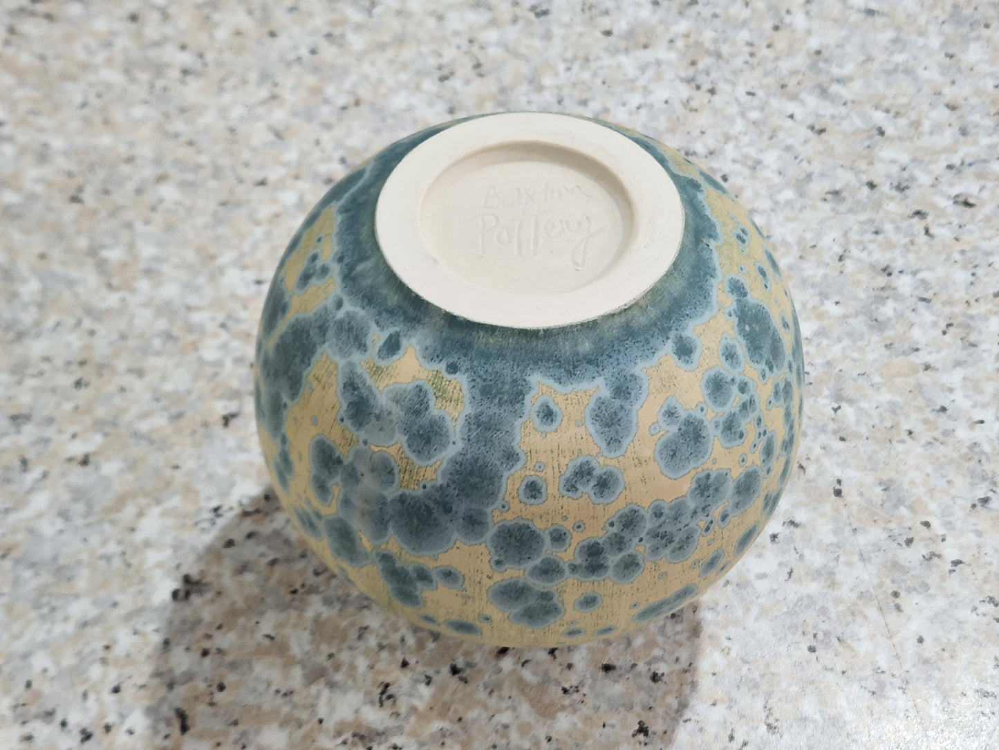 Base view of handmade ceramic vase showing Buxton Pottery stamp and teal crystalline glaze over cream matte background