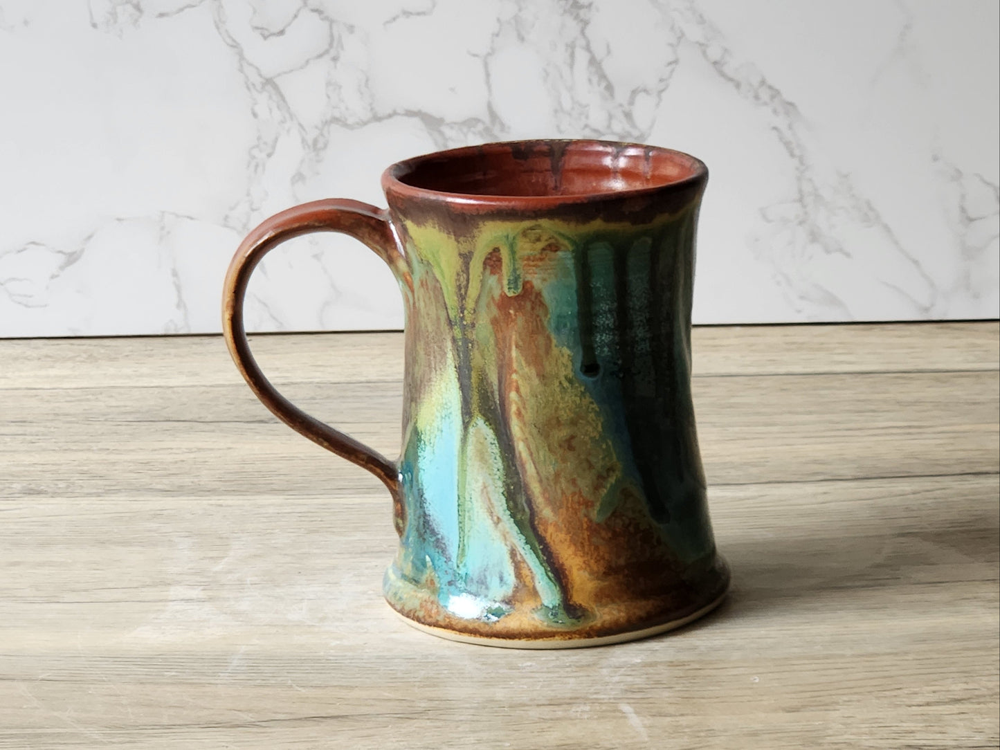 Handmade ceramic coffee mug with green and blue glaze on timber table