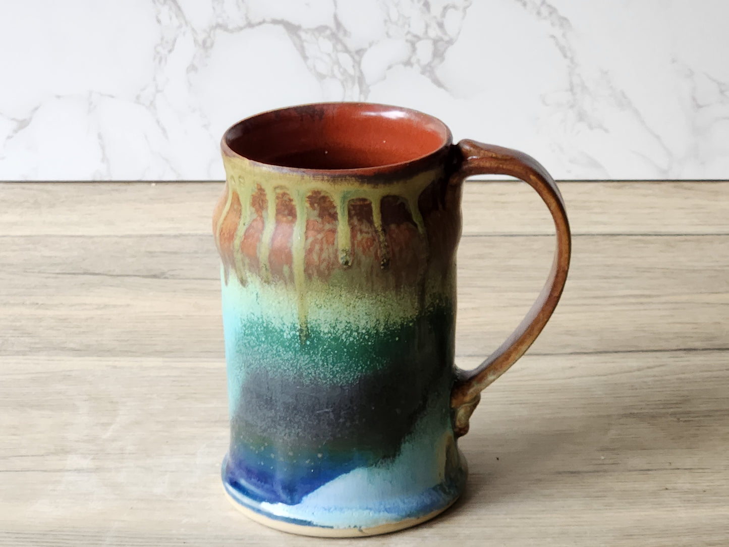 Wheel-thrown pottery mug with earthy drip glaze and warm rust interior