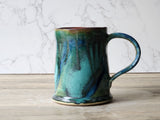 Side view of handmade ceramic coffee mug with curved handle and glossy multitone glaze