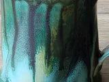 Detail of drippy glaze on handmade pottery mug with teal and earthy tones