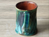 Rustic handmade pottery mug with curved handle and layered green glaze