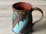 Wheel-thrown pottery mug close-up showing glossy turquoise glaze with earthy copper rim