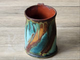 Artisan handmade mug with blue-green glaze and warm rust interior, studio product photo