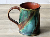 Handmade stoneware mug with curved handle and multicolour glaze, close-up on tabletop