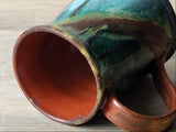 Close-up of handcrafted ceramic mug rim and interior with copper tones and reactive glaze