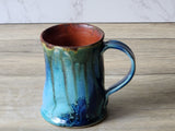 Side view of handmade pottery mug with green teal glaze and curved handle