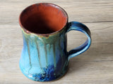 Handmade stoneware mug with layered teal glaze and warm rust interior
