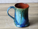 Wheel-thrown ceramic mug with curved handle and multitone green glaze finish