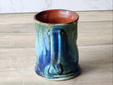Handmade ceramic tea mug with glossy teal glaze and warm rust interior