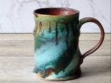 Handmade pottery coffee mug with glossy green and teal glaze, brown handle