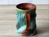 Rustic ceramic tea mug with mottled green teal glaze and warm red interior