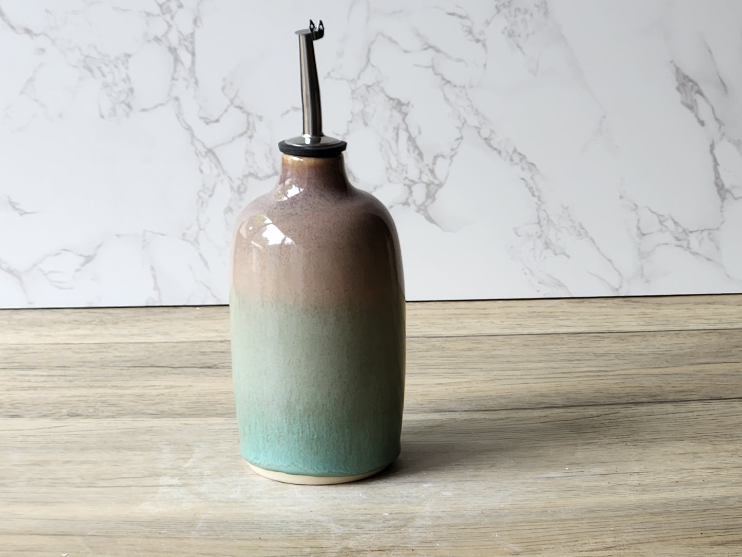 Green and brown handmade ceramic oil bottle with glossy glaze, photographed on neutral background