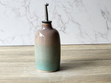 Green and brown handmade ceramic oil bottle with glossy glaze, photographed on neutral background