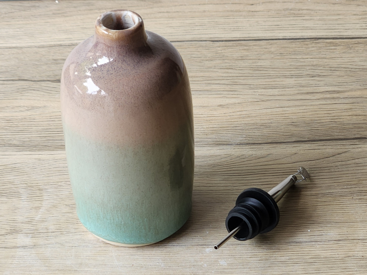 Close-up of green and brown glazed ceramic oil bottle showing glossy finish and colour variation