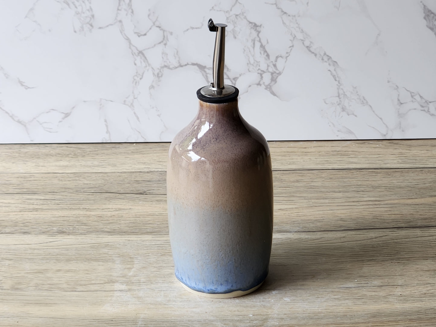 Ceramic olive oil dispenser bottle with stainless steel spout on timber surface