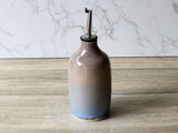 Ceramic olive oil dispenser bottle with stainless steel spout on timber surface